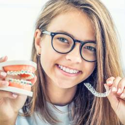 Orthodontics – Clear Aligners. braces and traditional braces on model in the hands of a young smiling girl.